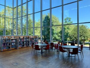 Ljust bibliotek med bokhyllor, bord och stora fönster mot grönska
